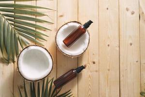 folha tropical, cosméticos de cuidado e coco em uma mesa de madeira. vista do topo. meios para cabelo, corpo, pele. flatlay foto
