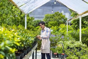 jardineiro asiático está cortando sua planta de flores no centro de jardim do viveiro para o conceito de cultivador de plantas nativas e exóticas foto