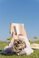 mulher mentindo e lendo seu livro favorito em um prado coberto de grama verde fresca em um dia ensolarado de verão ou primavera. foto