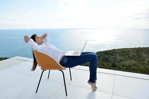 jovem relaxada em casa trabalhando no laptop foto