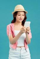 retrato de menina bonita, charmosa e atraente com telefone inteligente nas mãos, verificando e-mail, usando internet 5g, digitando sms, de pé sobre fundo azul foto