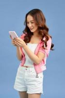 linda jovem asiática gosta de comunicação online, digitando texto isolado na parede azul do estúdio