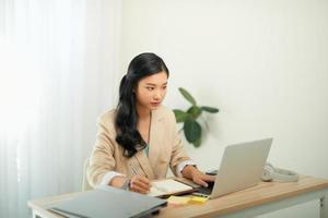 mulher jovem e bonita em roupas casuais usando laptop e sorrindo enquanto trabalhava dentro de casa foto
