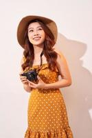 retrato de jovem sorridente alegre tirando foto com inspiração e usando vestido de verão. garota segurando a câmera retro. modelo posando em fundo bege com chapéu
