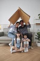 família tailandesa asiática, pai adulto, mãe e crianças pequenas brincando alegremente em uma sala de estar branca, casa de segurança de papelão construída com imaginação, fim de semana adorável e estilo de vida doméstico de bem-estar. foto