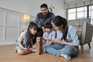 feliz asiático adorável atividade familiar tailandesa, pais, pai, mãe e filhos se divertem brincando e alegres blocos de brinquedo de madeira juntos no chão da sala de estar, fim de semana de lazer e estilo de vida de bem-estar doméstico. foto