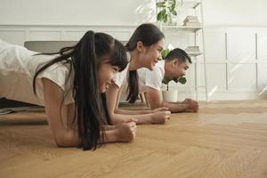 pais tailandeses asiáticos e filha exercício de treinamento de fitness e prática de ioga no chão da sala de estar, adorável remo juntos para saúde e bem-estar e estilo de vida doméstico feliz no fim de semana em família. foto