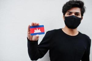 homem asiático usar todo preto com máscara facial segurar a bandeira do camboja na mão isolada no fundo branco. conceito de país coronavírus. foto