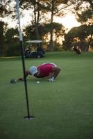 jogador de golfe soprando bola no buraco com pôr do sol no fundo foto