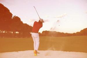 golfista acertando um bunker de areia no pôr do sol foto