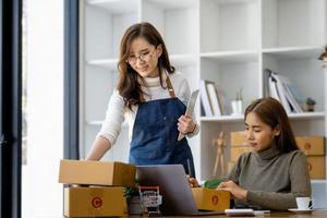 duas mulheres felizes vendendo produtos online. comece um pequeno empresário com uma caneta para anotar os endereços dos clientes e prepará-los para postagem. foto