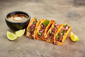 tradicional birria mexicana consome sopa e quatro tacos com carne estufada foto