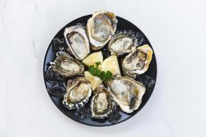 ostras frescas frutos do mar em um fundo de placa preta - concha de ostra aberta com ervas especiarias limão alecrim servido mesa e gelo frutos do mar saudáveis jantar de ostras cruas no restaurante comida gourmet foto