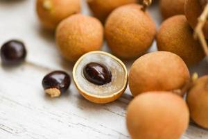 frutas tropicais longan frescas na tailândia - close-up casca de dimocarpus longan e sementes de frutas exóticas em fundo de madeira de mesa branca foto