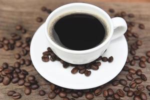xícara de café e grãos de café na mesa - café preto em caneca branca sobre fundo de madeira foto