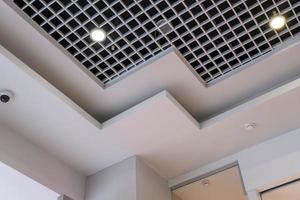 teto suspenso e grade com lâmpadas de halogênio e construção de drywall em sala vazia em loja ou casa. tecto falso branco e forma complexa. foto