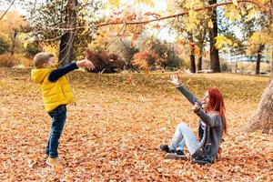 mãe e filho brincalhões se divertindo enquanto jogava folhas de outono. foto