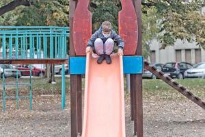 garotinho usando máscara facial enquanto desliza no parque. foto