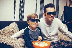 menino e seu pai assistindo filme 3d em casa. foto