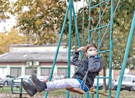 menino balançando no playground e usando máscara protetora. foto