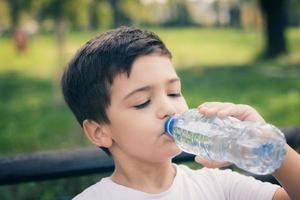 criança pequena se refrescando com água da garrafa de plástico. foto