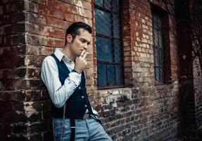 homem de estilo retrô pensativo fumando cigarro ao ar livre. foto