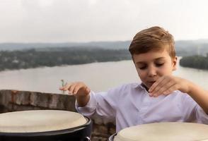 menino se divertindo enquanto joga bongôs ao ar livre. foto