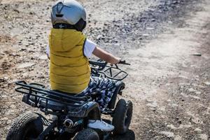 vista traseira do menino dirigindo o veículo atv na pista off-road. foto