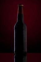 garrafa de cerveja com gotas sobre fundo vermelho escuro.