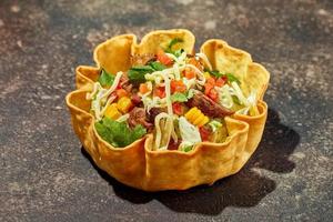 salada de taco em tigela de tortilha com carne, queijo, milho e alface foto