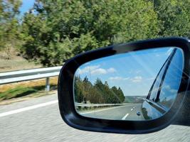 paisagem e reflexão da estrada no espelho retrovisor do carro preto. foto
