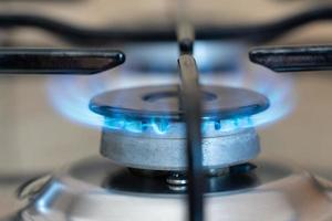close-up de um fogão a gás com gás saindo e queimando. o forno está ligado. a chama brilha azul. foto