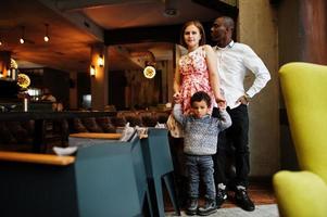 feliz família multiétnica com menino passa tempo no restaurante. relacionamentos de homem africano e mulher branca europeia. foto