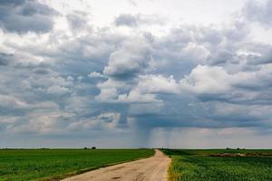 paisagem com céu escuro com nuvens de chuva antes da tempestade em campo verde com estrada de cascalho. frente de trovoada foto