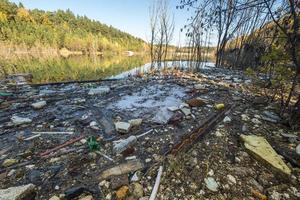 montes de resíduos de construção, lixo doméstico, espuma e garrafas plásticas na margem de um lago florestal, problemas de poluição ambiental foto