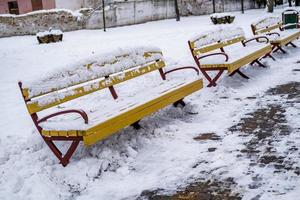 bancos de parque de madeira amarelos cobertos de neve foto