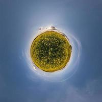 planeta minúsculo amarelo no campo de colza no céu azul com belas nuvens. transformação do panorama esférico 360 graus. vista aérea abstrata esférica. curvatura do espaço. foto