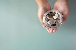 mãos adultas segurando uma jarra com moedas no conceito de poupança e doação foto