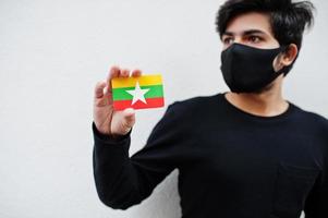 homem asiático usar todo preto com máscara facial segurar a bandeira de mianmar na mão isolada no fundo branco. conceito de país coronavírus. foto