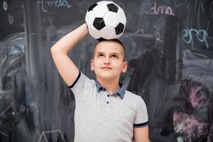 menino feliz segurando uma bola de futebol na cabeça foto