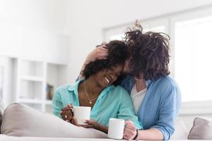 casal multiétnico sentado no sofá em casa bebendo café foto