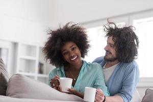 casal multiétnico sentado no sofá em casa bebendo café foto