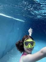 criança sorridente em óculos nadar, mergulhar na piscina com diversão - pular profundamente debaixo d'água. estilo de vida saudável, atividade de esportes aquáticos de pessoas nos verões. foto