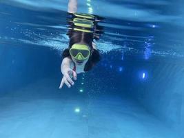 criança sorridente em óculos nadar, mergulhar na piscina com diversão - pular profundamente debaixo d'água. estilo de vida saudável, atividade de esportes aquáticos de pessoas nos verões. foto