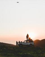 grupo de criadores de conteúdo de viajantes fica ao lado do veículo 4wd juntos ao ar livre na aventura da natureza assiste ao pôr do sol sobre o horizonte sobre a paisagem de nuvens no deserto. exploração e aventura foto