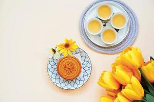 postura plana de bolo de lua chinês com chá quente e flor no conceito de fundo amarelo, feriado e festival foto