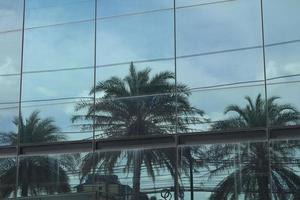 edifício de vidro alto refletindo as palmeiras usadas para decorar o jardim e o céu azul no início da manhã é lindo em um dia quente e ensolarado pela manhã. foto