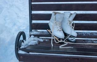 patins brancos estão em um banco de madeira marrom. férias de inverno ativas, estilo de vida saudável foto