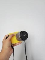 uma mão está segurando uma câmera canon eos m10, esta câmera recebe um protetor de borracha amarelo. foto