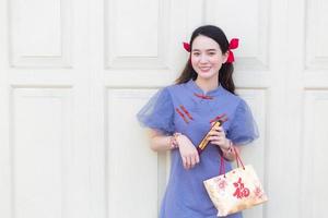 mulher asiática de vestido chinês azul-cinza segura o saco de papel que rastreou a palavra que significa feliz em chinês e fica na porta de madeira branca como pano de fundo. foto